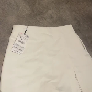Oanvänd Vit kjol med inbyggda shorts från Zara - Snygg vit kjol från Zara i en stilren design. Kjolen har en kort längd med skorts  och är perfekt för en chic look. Den är tillverkad i ett mjukt material som ger en bekväm passform.