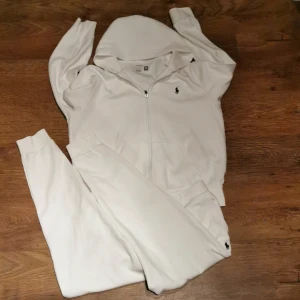 Vit hoodie från Polo Ralph Lauren - Säljer en stilren vit hoodie från Polo Ralph Lauren. Den har en dragkedja framtill och en klassisk broderad logga på bröstet. Perfekt för en avslappnad stil. Byxor och hoodie kommer med!! 