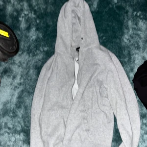 Grå hoodie från Jack and Jones  - Säljer en stilren grå hoodie med lång ärm och klassisk design. Perfekt för en avslappnad look. Den har en praktisk huva och är tillverkad i ett mjukt material för extra komfort.