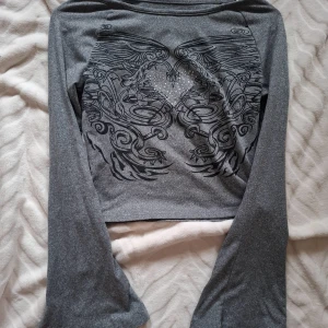 Grå långärmad tröja med hjärtmönster - Snygg grå långärmad tröja med ett detaljerat svart mönster och glittrande stenar i form av ett hjärta på framsidan 💕 lite cropped! Köpt på antingen Shein eller temu kommer inte ihåg! Använde kanske 2 gånger? 😜 Färgen är mest sann på den första bilden! 🙌