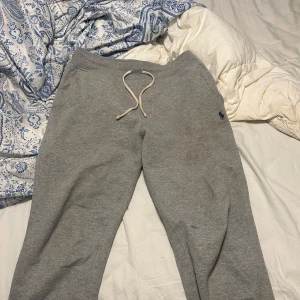 Grå mjukisbyxor från Polo Ralph Lauren - Säljer ett par grå mjukisbyxor från Polo Ralph Lauren med en broderad logga i mörkblått. Byxorna har snörning i midjan och en bakficka. Perfekta för en avslappnad stil.