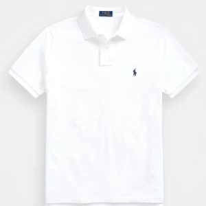 Vit pikétröja från Ralph Lauren - Säljer en klassisk vit pikétröja från Ralph Lauren med den ikoniska loggan broderad på bröstet. Tröjan har korta ärmar och en stilren krage med knappar. Perfekt för en avslappnad och stilren look.