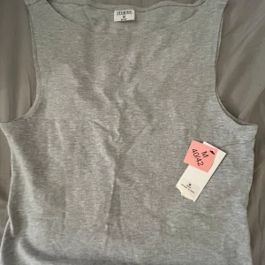 Grå ärmlös topp  - Säljer en stilren grå ärmlös topp från Stories i storlek M. Perfekt för en minimalistisk look. Toppen har en enkel design och är gjord i ett mjukt material.