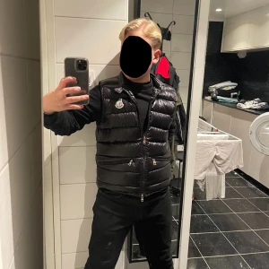 Moncler väst säljes 🏌️‍♂️ - Säljer denna sjukt snygga svarta dunvästen  från Moncler med en glansig finish och dragkedja framtill. Västen är storlek 1, dvs S. Västen har två praktiska fickor med dragkedja. Skick 9/10 finns inga spår av trasigheter. Pris är inte skrivet i sten. Kan även bytas mot moncler cardigan eller andra schyssta plagg. Skriv för fler frågor.