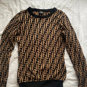 Svart och beige mönstrad tröja från Fendi - Snygg svart och beige tröja från Fendi med det ikoniska FF-mönstret. Tröjan har långa ärmar och en rund halsringning. Perfekt för att ge din outfit en lyxig touch (använd endast en gång)🩷