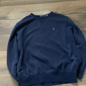 Mörkblå tröja från Polo Ralph Lauren - Säljer en stilren mörkblå tröja från Polo Ralph Lauren med det klassiska röda logotypbroderiet på bröstet. Tröjan har långa ärmar och en rund halsringning. Perfekt för en soft och laidback look.