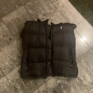 Svart dunväst med dragkedja rhalp lauren - Säljer en stilren svart dunväst med dragkedja. Perfekt för kyligare dagar och enkel att matcha med olika outfits. Västen har praktiska fickor med dragkedjor för säker förvaring.