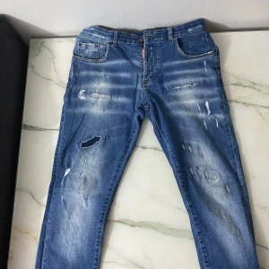 Blå jeans med slitningar - Snygga blå jeans från Dsquared2 med coola slitningar och distressed detaljer. De har en klassisk femficksdesign och knappgylf. Perfekta för en avslappnad stil med en touch av edge.