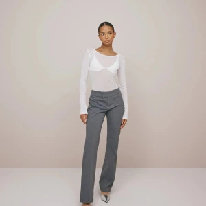 Grå low waist kostymbyxor - Snygga grå kostymbyxor med låg midja och bootcut-stil. Byxorna har en stilren design med knappar och dragkedja framtill. Knappt använda, första bilden är lånad från nellys hemsida 