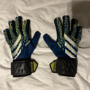 Adidas Predator målvaktshandskar - Säljer ett par Adidas Predator målvaktshandskar i blått och svart med vita detaljer. Handskarna har en justerbar handledsrem för bättre passform och grepp. Perfekta för fotbollsmatcher och träning. 🧤⚽ 