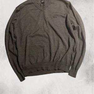 Boss pullover - Säljer en stilren grå tröja från Boss med v-ringning och broderad logga på bröstet. Tröjan har långa ärmar och är tillverkad i ett mjukt material som passar perfekt för kyligare dagar. Perfekt för dig som vill ha en klassisk och tidlös look. Xl barn. S herr. Inga defekter. Kom privat för fler frågor!💫