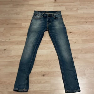 Skit snygga Nudie Jeans! - Snygga blå jeans från Nudie Jeans med klassisk femficksdesign och orange sömmar. De har en slim passform och är tillverkade i slitstarkt denim. Perfekta för en avslappnad stil. Har kollat igenom jeansen och ingen typ av slitage, De kostar ca 1600 nypris och är inte mycket använda