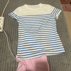 Vit och blå randig t-shirt - Säljer en fräsch vit och blå randig t-shirt med korta ärmar. Perfekt för en avslappnad stil. Passar bra till jeans eller shorts för en somrig look.