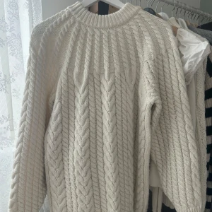 Vit stickad tröja från H&M - Säljer en mysig vit stickad tröja från H&M med ett klassiskt flätmönster. Tröjan har långa ärmar och ribbstickade muddar vid ärmslut och nederkant. Perfekt för kyliga dagar! ❄️