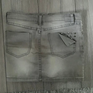 Grå jeanskjol med nitar - Snygg grå jeanskjol med nitar på fickorna. Kjolen har en tight passform och är kort i modellen. Perfekt för en trendig look.