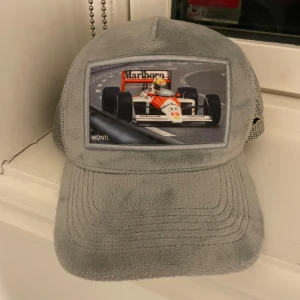Grå keps med racingmotiv - Snygg grå keps från Ted Wonti med ett coolt racingmotiv på framsidan. Kepsen har ett nätmaterial på sidorna och baksidan för extra ventilation. Perfekt för racingfans som vill ha en stilren accessoar.