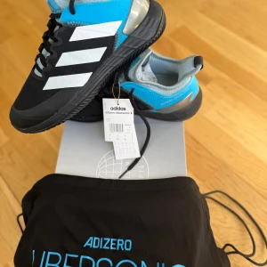 Adidas Adizero Ubersonic 4 - Helt oanvänt par adidas adizero ubersonic 4.  Nypris 1595kr. De kommer med en praktisk förvaringspåse.