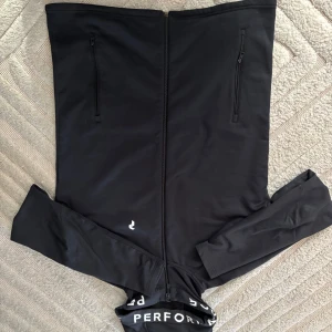 Peak Perfomance - Säljer en stilren svart jacka med lång ärm och dragkedja framtill. Jackan har två praktiska fickor med dragkedjor och en diskret logga på framsidan. Perfekt för en sportig look.