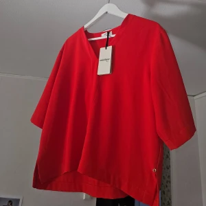 Röd topp från Ottod'Ame - Säljer en snygg röd topp från Ottod'Ame med trekvartsärmar och en stilren design. Perfekt för att liva upp garderoben med en färgklick. Toppen har en enkel och elegant look som passar till många tillfällen.