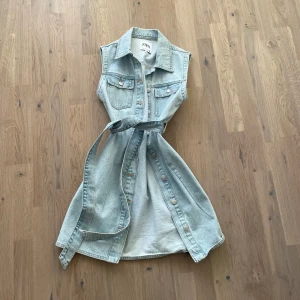 Ljusblå ärmlös jeansklänning från Zara - Snygg ljusblå jeansklänning från Zara med knappar framtill och ett matchande bälte i midjan. Klänningen är ärmlös och har två bröstfickor för en cool look. 