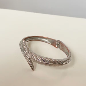 Silverfärgat armband med vriden design - Snyggt silverfärgat armband med en unik vriden design. Armbandet har en elegant och stilren look som passar perfekt för att lyfta vilken outfit som helst. Perfekt för dig som gillar att sticka ut med dina accessoarer.