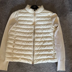 Kräm vit cardigan från Moncler - Säljer en stilren vit cardigan från Moncler med quiltad framsida och långa ärmar. Jackan har en dragkedja framtill och Moncler-logga på ärmen. Skick 9/10 men såklart pris efter skick, Perfekt för kyligare dagar när du vill hålla stilen. 🧥✨passar mindre 