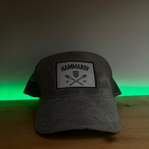 Hammarby Truckerkeps Grå - Snygg grå keps med broderad Hammarby-logga framtill. Kepsen har ett nätmaterial på baksidan och justerbar rem för perfekt passform. Perfekt för att visa ditt stöd för laget!