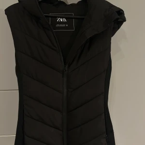 Svart dunväst från Zara - Snygg svart dunväst från Zara med dragkedja framtill. Perfekt för lager-på-lager under kyliga dagar. Västen har en stilren design och är lätt att matcha med olika outfits.