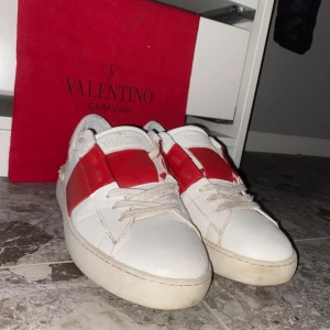 Valentino Garavani sneakers i vitt och rött - Snygga Valentino Garavani sneakers i vitt med röda detaljer. Skorna har en klassisk design med snörning och rund tå. Perfekta för att ge din outfit en lyxig touch. Väldigt bra skick och passar till allt. 