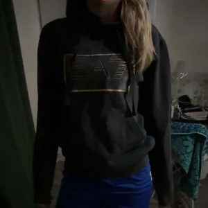 Svart vintage hoodie från Emporio Armani - Säljer en svart hoodie från Emporio Armani med EA7-logga i guld på bröstet (Äkta). Det står tyvärr ingen storlek men är som en xs/s.