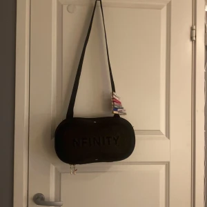 Svart glittrig axelväska från Nfinity  - Säljer en svart axelväska från Nfinity med ett stilrent och sportigt utseende. Väskan har en präglad logotyp och en praktisk dragkedja. Perfekt för att bära dina nödvändigheter med stil❤️
