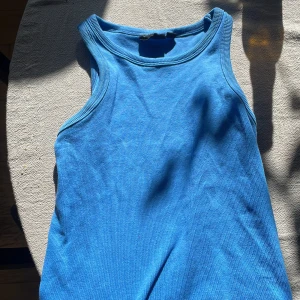 Blå ribbad linnetopp - Säljer en snygg blå ribbad linnetopp. Perfekt för varma dagar med sin ärmlösa design och bekväma passform. Toppen har en klassisk rund halsringning och är gjord i ett mjukt material.