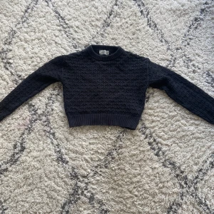 Svart stickad tröja från H&M - Säljer en svart stickad tröja från H&M med ett snyggt hålmönster. Tröjan har långa ärmar och ribbade muddar vid ärmslut och nederkant. Perfekt för en stilren look.