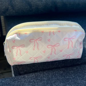 Vit quiltad necessär med rosa rosetter - Söt vit necessär med quiltat mönster och rosa rosetter samt hjärtan. Perfekt för att förvara smink eller andra småsaker. Den har en praktisk dragkedja upptill.