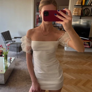 Studentklänning med puffärmar - Säljer en elegant vit axelbandslös klänning med puffiga, transparenta ärmar. Klänningen är kort och figurnära, perfekt för en stilren look💕💕