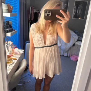 Ljusrosa  klänning med v-ringning - Säljer en söt vit klänning med djup v-ringning och plisserad kjol. Klänning är väldigt kort men kan användas över jeans också som en lång topp vilket är gulligt, eller till ett par shorts