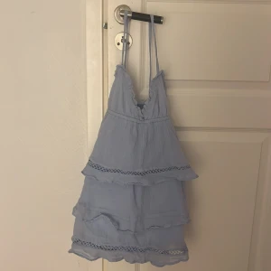 Ljusblå klänning med volanger - Charmig ljusblå klänning med volanger och spetsdetaljer. Axelbandslös design med flera lager som ger en luftig känsla. Perfekt för varma dagar.