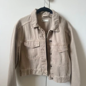 Beige jeansjacka från Ginatricot - Säljer en snygg beige jeansjacka från Ginatricot. Jackan har en klassisk design med knappar framtill och två bröstfickor. Perfekt för våren! Det är en croppad cool design och sitter normalt, endast använd 2 gånger❤️