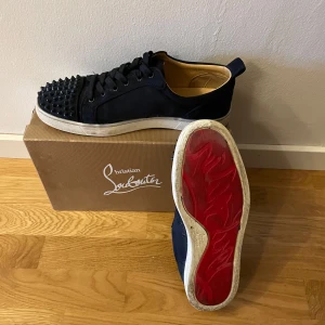 Svarta sneakers med nitar från Christian Louboutin - Snygga svarta sneakers från Christian Louboutin som är mörkblå med ikonisk röd sula och nitar på tån. Skick 8.5-10 så väldigt bra skick. Storlek 44. Boxen följer med. Priset kan diskuteras vid snabbaffär.