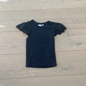 Svart topp med spetsärmar från Gina Tricot - Säljer en stilren mörkblå topp från Gina Tricot med vackra spetsdetaljer på ärmarna. Perfekt för att ge en elegant touch till din outfit. Toppen har en normal passform och är tillverkad i ett mjukt material.