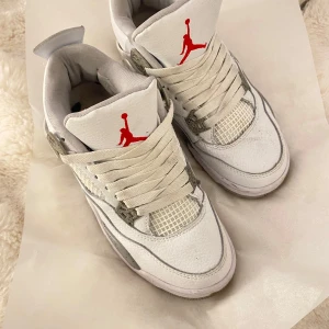 Vita Nike Air Jordans med grå detaljer - Säljer ett par vita Nike Air Jordans med grå detaljer och röd logga. Skorna har snörning och en rund tå. Perfekta för sneakerheads som vill ha en klassisk stil.