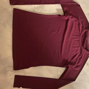 Träning tröja - Säljer en stilren vinröd långärmad tröja. Perfekt för kyligare dagar och enkel att matcha med andra plagg. Tröjan har en rund halsringning och är gjord i ett mjukt material.