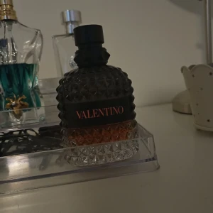 Parfym från Valentino, tar byten, ungefär 50 ml kvar - Elegant parfymflaska från Valentino med en lyxig design. Flaskan har en mörk, facetterad yta med en svart etikett och röd text. Perfekt för den som vill ha en sofistikerad doftupplevelse.