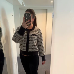 Svartvit rutig kofta - Säljer en stilren svartvit rutig kofta med svarta muddar och detaljer. Koftan har långa ärmar och fickor på bröstet. Perfekt för en chic och avslappnad look.