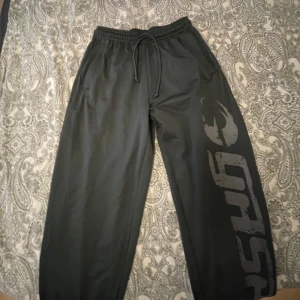 Gråa mjukisbyxor med tryck - Säljer ett par gråa mjukisbyxor med ett stort tryck längs benet. Byxorna har en elastisk midja med dragsko för justerbar passform. Perfekta för en avslappnad stil. Den kan användas till Gymmet som en perfekt idé. Väldigt mysiga och stretchiga.