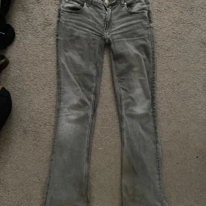 Grå bootcut jeans från Gina Tricot - Snygga grå bootcut jeans från Gina Tricot i storlek 164. Perfekta för en avslappnad stil med en klassisk femficksdesign och knappgylf. De har en lätt tvättad look som ger en cool vintagekänsla.