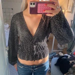 Svart och vit prickig blus - Säljer en snygg svart blus med vita prickar. Blusen har en v-ringad design och långa ärmar. Den är croppad med en elastisk midja som ger en fin passform. Perfekt för en stilren look! Från Zara i storlek S💗