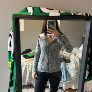 Grå hoodie med dragkedja - Säljer en grå hoodie med dragkedja och lång ärm. Perfekt för en kall kväll. Den har en bekväm passform och är idealisk för kyligare dagar. Ull inuti.