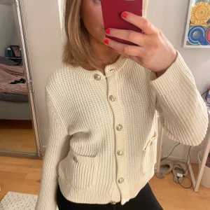 Vit stickad kofta med knappar - Säljer en stilren vit stickad kofta med guldiga knappar framtill som gör den lite lyxigare. Har använt som mest två gånger så i fint skick! 🧡 Är på bilden en liten sminkfläck i halsringningen som är borttvättad nu! 