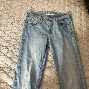 Ljusblå jeans med stjärndetaljer från Levi's - Snygga ljusblå jeans från Levi's med coola stjärndetaljer på framsidan. Klassisk femficksdesign och knappgylf. Perfekta för en avslappnad stil med en touch av unikhet.